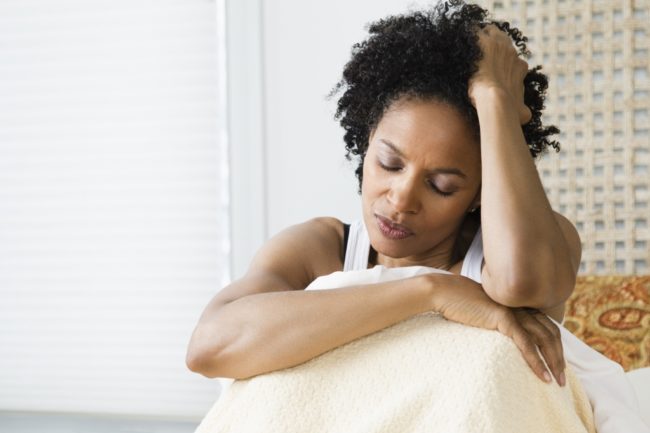 Mid adult woman sitting on the bed and suffering from a headache