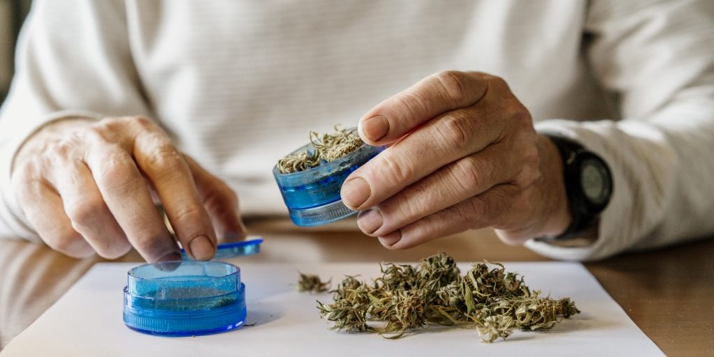 Midsection of senior man grinding weed in grinder at home