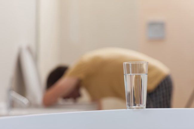 Glass of dissolving medicine with vomiting man in background