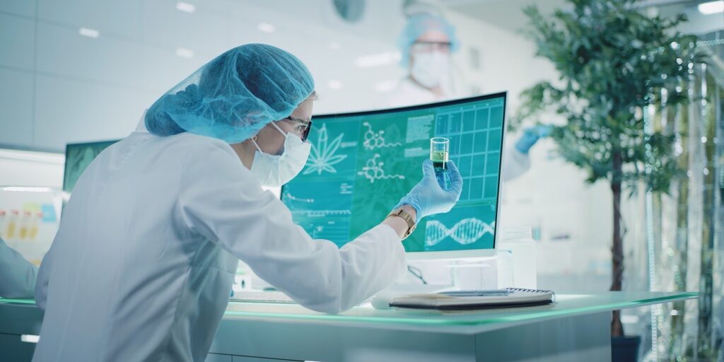 Female scientist testing medical marijuana, making notes. Team working in background. Charts and models on computer screens. Modern laboratory interior